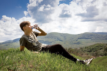 The guy sits on a mountain and drinks water from a bottle. mountain landscape.