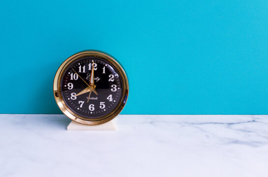Vintage antique wind up alarm clock on a white table with a bright blue background