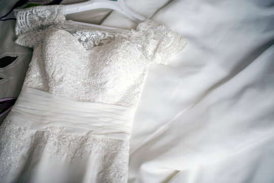 Vestido de novia blanco con encaje, de manga corta, en una percha estirado sobre la cama. Vista desde arriba.