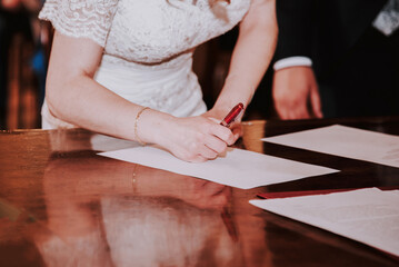 Una mujer vestida de blanco firma un papel. Concepto de firmar los papeles de la boda en una ceremonia civil. Novia renovando sus votos. - obrazy, fototapety, plakaty