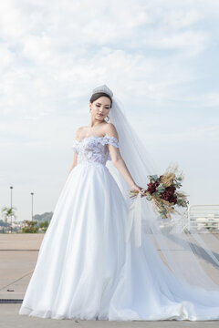 Uma jovem mulher usando um vestido de noiva com c&eacute;u nublado ao fundo.