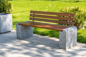 Wooden bench with stable granite base in city square or park. Empty place to rest next to footpath....