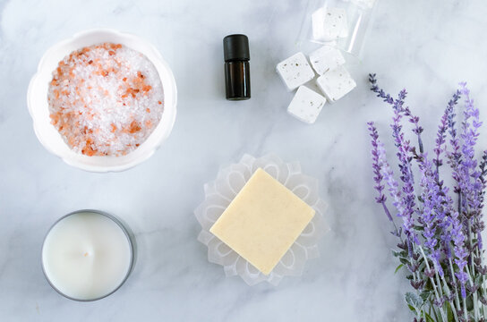 Overhead Flat Lay Of Self Care Items, Soap, Bath Salts, Candle, Essential Oil And Lavender Plant On A White Background