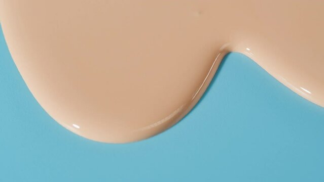 Flowing foundation tone on blue background. Brown cream texture close-up. Makeup and beauty products concept, cosmetics, eyeshadow palette, bronzer or concealer.