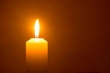 A single burning candle flame or light glowing on a yellow candl