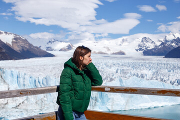 A girl in a warm green jacket admires a prominent view of the beautiful Perito Moreno glacier and Lake Argentina