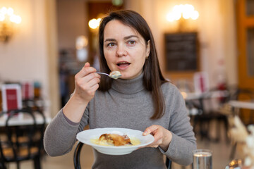 Woman enjoying slice of traditional apple strudel with vanilla sauce in coffee house while...