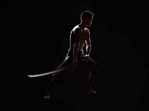 The Spirit of the Samurai. Silhouette of an Asian man holding a sword in the lower position on a dark background. 3D illustration.