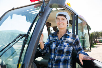 Portrait of mature female worker sitting in tractor on farm