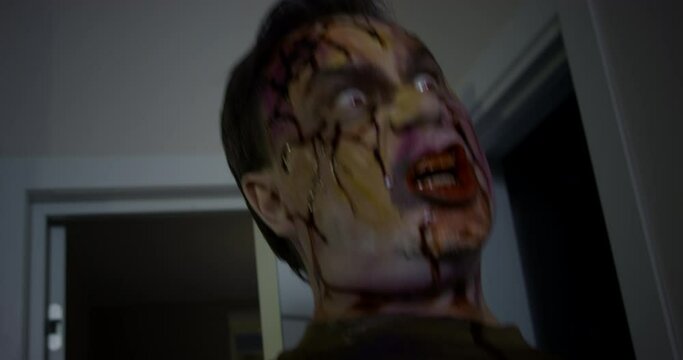 Spooky dead man with blood covering face and mouth screams looking for food in apartment. Zombie with blood stains and traces looks for victim closeup