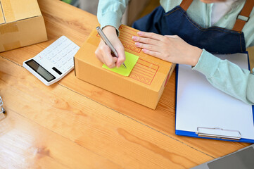 Female online shopping store owner writing a customer address on the box.