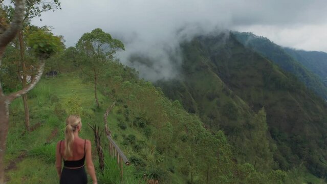 Caucasian blond woman hiking along edge of viewpoint looking at lake Batur, aerial