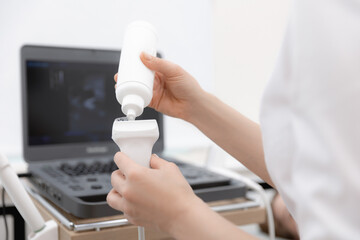 Closeup hands of woman doctor preparing for ultrasound device scan. Gynecologist applies gel on...