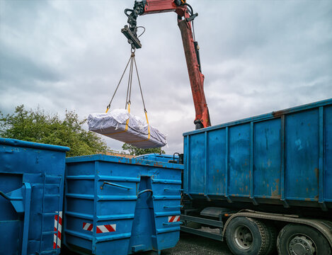 Crane truck with asbestos bag being reloaded into another container at a recycling yard.