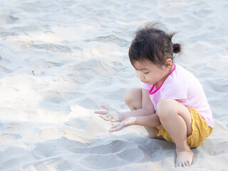 Positive charming 4 years old cute baby Asian girl, little preschooler child playing on sand beach on beautiful sunny day in summer time