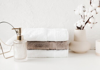 Fototapeta na wymiar Spa, bathroom background. Towels on white desk near white wall and interior accessories with copy space. Neutral beige colors.