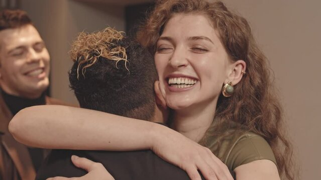Medium slowmo of young beautiful Caucasian woman with boyfriend wearing fancy clothes visiting their female friend, hugging in hallway while greeting each other