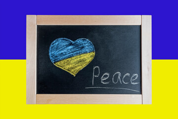 Flag of Ukraine and a heart drawn in chalk. Children write the text Peace on the blackboard with chalk.
