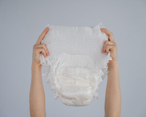 A woman holds an adult diaper on a white background. Incontinence problems.