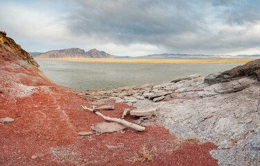 The shore of the Krasnoyarsk reservoir without water, red stones, clay and driftwood on the shore, rainy sky over Mount Tepsey Tepsey