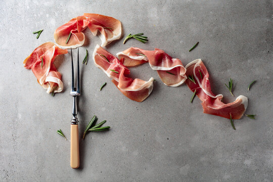 Prosciutto with rosemary on an old concrete background.