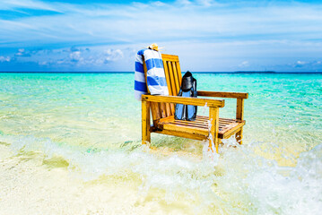 A wooden chair standing in the Indian Ocean with a towel, shell and flippers.