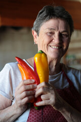 Happy portrait of an older housewife wearing her homemade apron and holding three different colored palermo peppers in her hands.