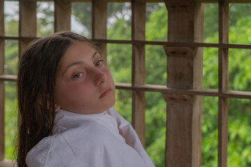 Portrait of a Little Caucasian Girl relaxing on a wooden balcony with green background wearing a white bathrobe 