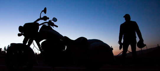 silhouette of a man approaching a motorcycle at sunrise or sunset 