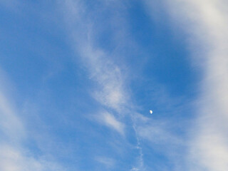 A small moon and high cirrus clouds in a blue sky. Beautiful sky background with high white clouds.