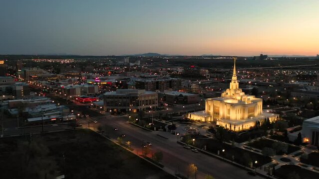 Wide drone orbit around mormon temple in Ogden Utah, brightly illuminated in dark city.