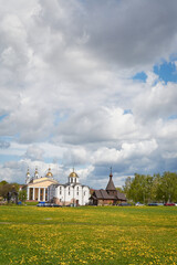 Spring urban landscape of a small town. In the foreground is a field of yellow dandelions, in the background are several churches. Most of the frame is occupied by an expressive cloudy sky.
