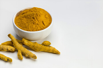 Turmeric tubers and ground turmeric in a white bowl. Close-up, studio shot.