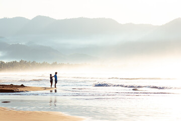Fototapeta na wymiar Couple in silhouette on the shore of the beach, enjoying the sunrise.