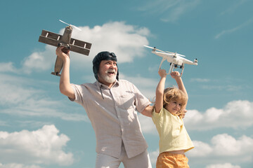 Young grandson and old grandfather hold plane and drone quad copter against sky. Child pilot...