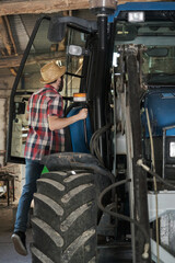 Young farmer climbing in a tractor in a barn. Agricultural industry.