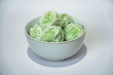 One of the traditional Indonesian snacks made from green glutinous rice and inside there is brown sugar, small round shape with grated coconut topping, served in a small bowl on a white background