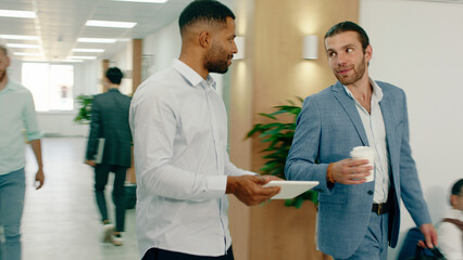 Obraz premium Two intelligent well known business men are walking through the office and talking while greeting everyone, they sit at a round table with a blue couch to talk about work