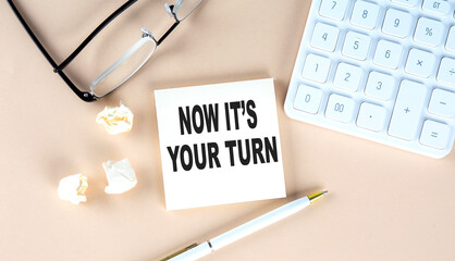NOW IT'S YOUR TURN text on sticky with pen ,calculator and glasses on beige background