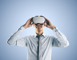 Virtual reality concept with young man gets new emotions in VR glasses on his head on abstract light blue background, close up, isolated