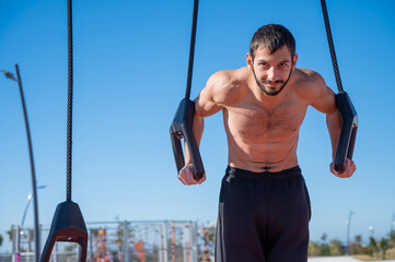 Shirtless man doing loop exercises outdoors. 