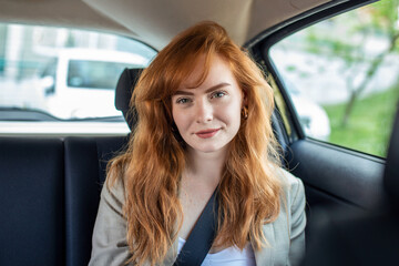 Beautiful young businesswoman sitting on back seat of a car and looking at the camera. Female business executive travelling by a cab.