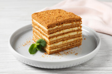 Slice of delicious layered honey cake with mint served on white wooden table