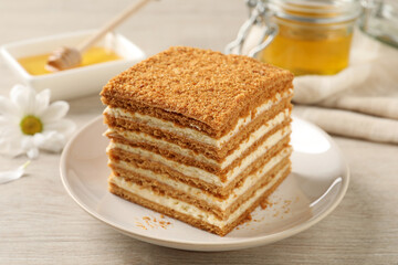 Slice of delicious layered honey cake served on wooden table, closeup