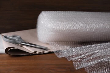 Scissors, paper and roll of bubble wrap on wooden table