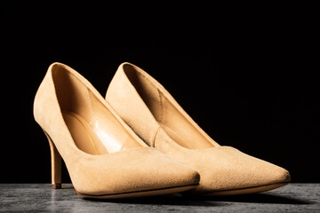 Cream-colored women's suede shoes with thin heels on a black background.