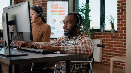 African american man in wheelchair answering helpline call at customer service job, working in...