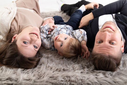Funny portrait of a young blond caucasian family with a small child lying on the floor. Look at camera.