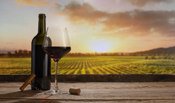 Charm. Still life with red wine glass and bottle on wooden table over background of panoramic view of lush vineyards at sunset. Tasting, festivals concept