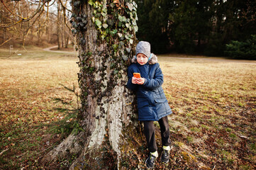 Fototapeta premium Boy looking at mobile phone at Valtice park, against big tree.